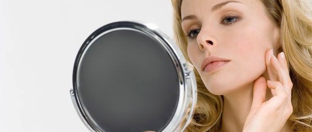 Young woman looking in mirror, touching face